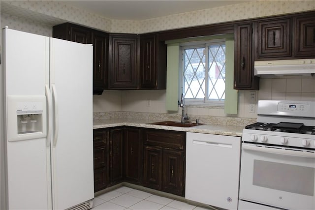 kitchen with dark brown cabinetry, white appliances, sink, and light tile patterned floors