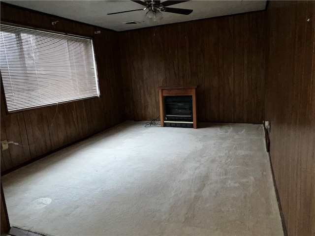 carpeted spare room with wooden walls, a fireplace, and ceiling fan