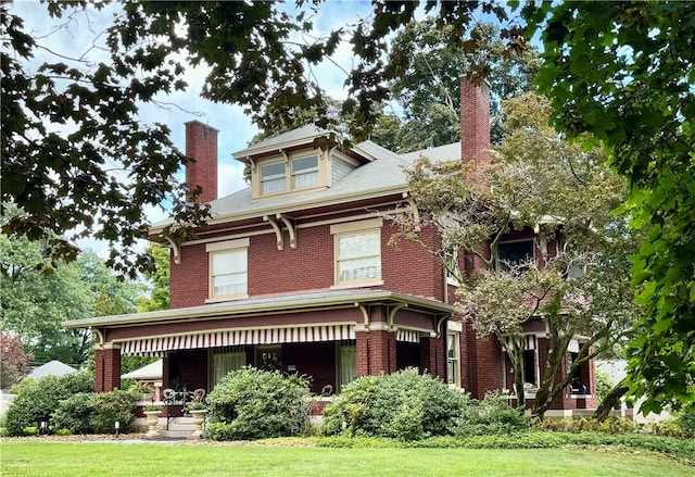 back of house featuring brick siding, a chimney, covered porch, and a yard