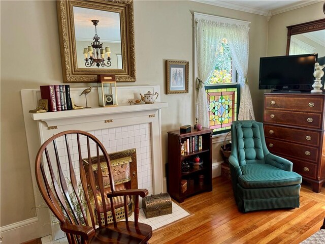 living area with a tile fireplace, hardwood / wood-style floors, crown molding, and a notable chandelier