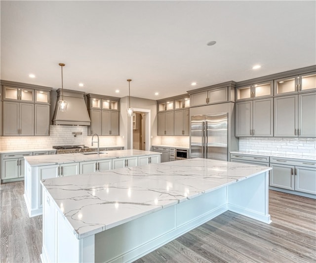 kitchen with custom range hood, a large island, pendant lighting, light hardwood / wood-style flooring, and built in fridge