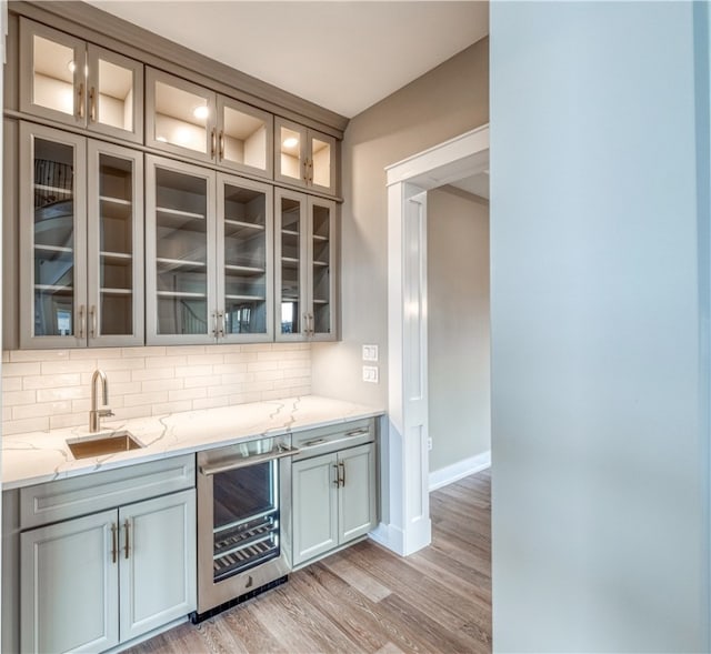 bar featuring backsplash, light stone counters, beverage cooler, sink, and light hardwood / wood-style flooring