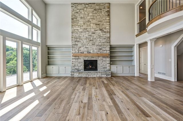 unfurnished living room with a stone fireplace, built in features, a high ceiling, and light hardwood / wood-style flooring