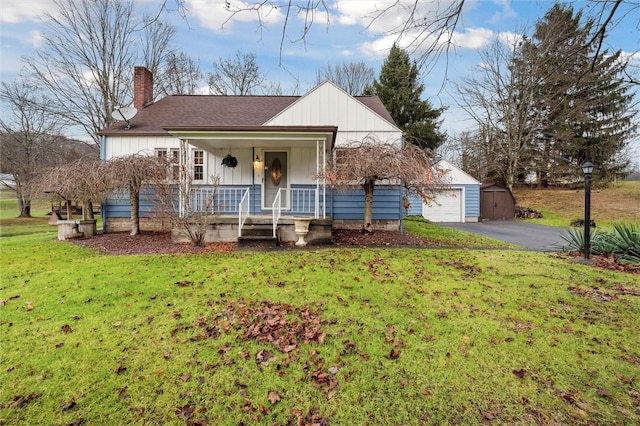 bungalow-style home with covered porch, a garage, an outdoor structure, and a front yard