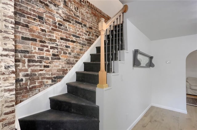 stairs with hardwood / wood-style flooring and brick wall