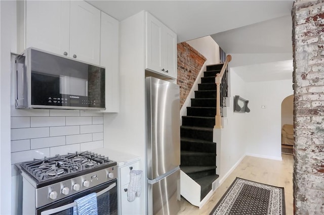 kitchen with backsplash, white cabinetry, stainless steel appliances, and light wood-type flooring