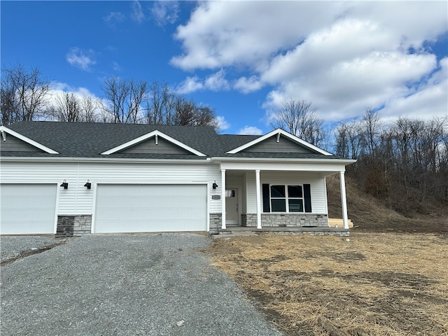 view of front of home with roof with shingles, covered porch, a garage, stone siding, and driveway