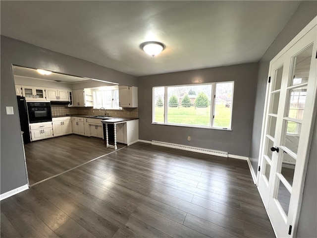 kitchen featuring tasteful backsplash, dark wood-type flooring, a baseboard radiator, white cabinets, and black oven