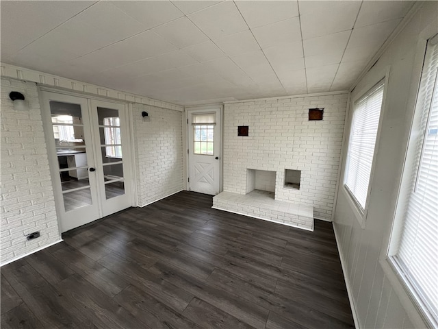 unfurnished living room featuring dark hardwood / wood-style flooring, brick wall, and french doors