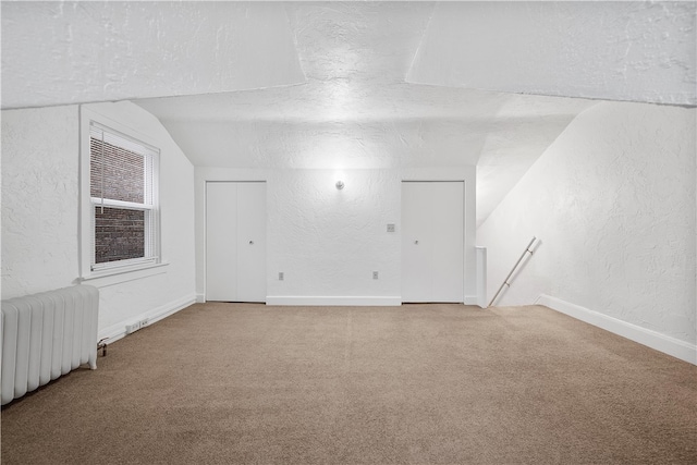 carpeted spare room with a textured ceiling, radiator heating unit, and vaulted ceiling