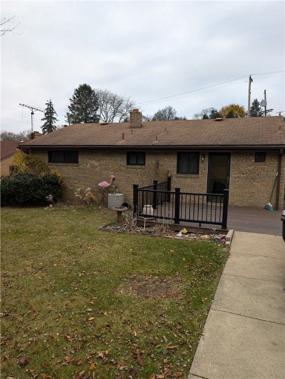 back of property featuring roof with shingles, a deck, a lawn, and brick siding