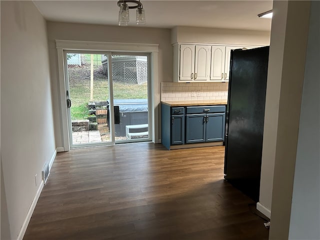 kitchen with backsplash, black fridge, white cabinets, and dark hardwood / wood-style floors