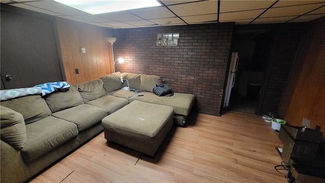 living room featuring a paneled ceiling, light hardwood / wood-style flooring, wood walls, and brick wall