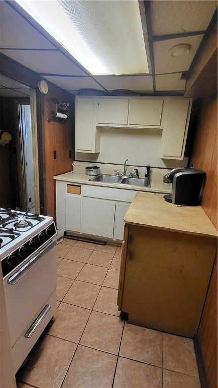 kitchen with stove, light tile patterned floors, wood walls, and sink