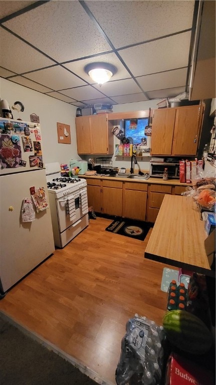 kitchen with a paneled ceiling, light hardwood / wood-style floors, gas range, sink, and white fridge