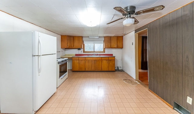 kitchen featuring wood walls, white refrigerator, stainless steel range with gas cooktop, sink, and ceiling fan