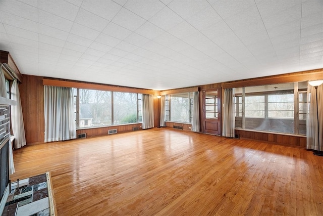 unfurnished living room featuring a stone fireplace, wood walls, and light hardwood / wood-style flooring