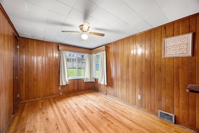 unfurnished room with wood walls, ceiling fan, and light hardwood / wood-style floors