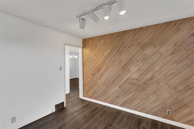 spare room featuring wood walls, dark hardwood / wood-style floors, and track lighting