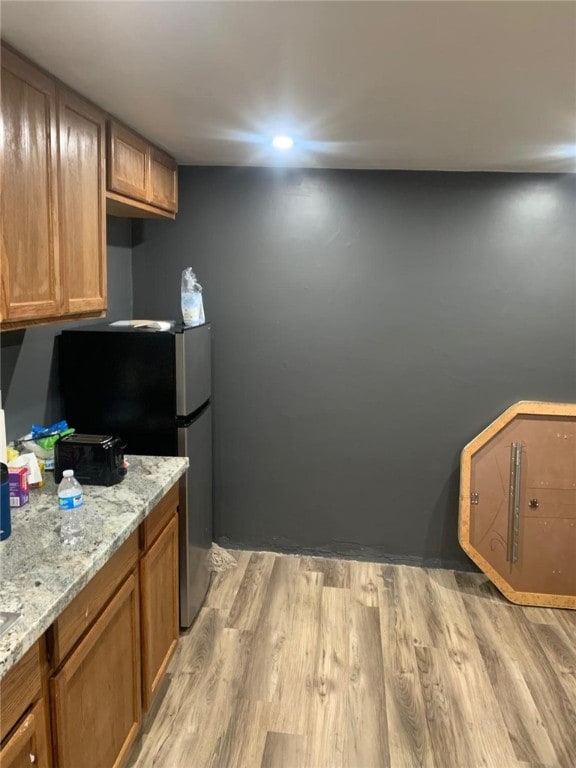 kitchen featuring stainless steel fridge, light stone counters, and light wood-type flooring