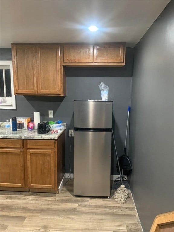 kitchen featuring stainless steel fridge, light stone counters, and light hardwood / wood-style flooring