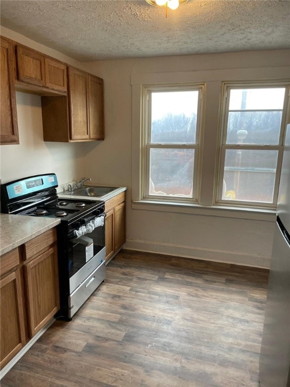 kitchen with a textured ceiling, sink, dark wood-type flooring, and stainless steel range oven