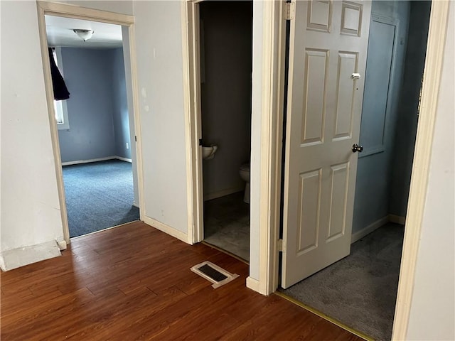 hall with baseboards, visible vents, and dark wood finished floors