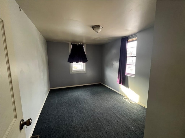 empty room featuring a healthy amount of sunlight, baseboards, visible vents, and dark colored carpet