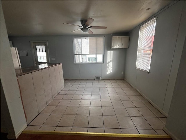 spare room featuring light tile patterned floors, visible vents, plenty of natural light, and a ceiling fan