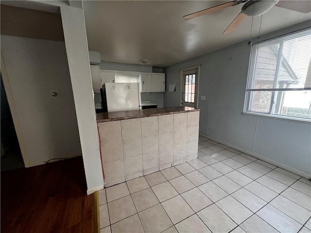 kitchen featuring a peninsula, a ceiling fan, white cabinets, freestanding refrigerator, and dark countertops