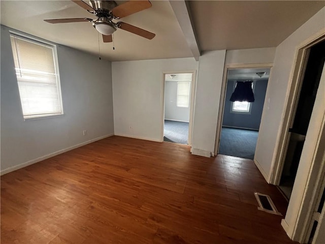 empty room featuring a healthy amount of sunlight, visible vents, dark wood finished floors, and baseboards