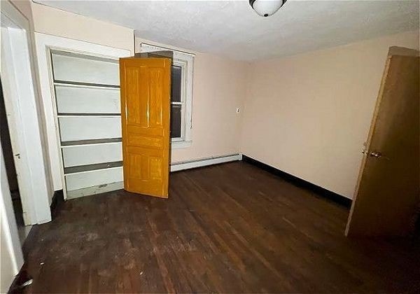 unfurnished bedroom with dark hardwood / wood-style floors and a baseboard heating unit