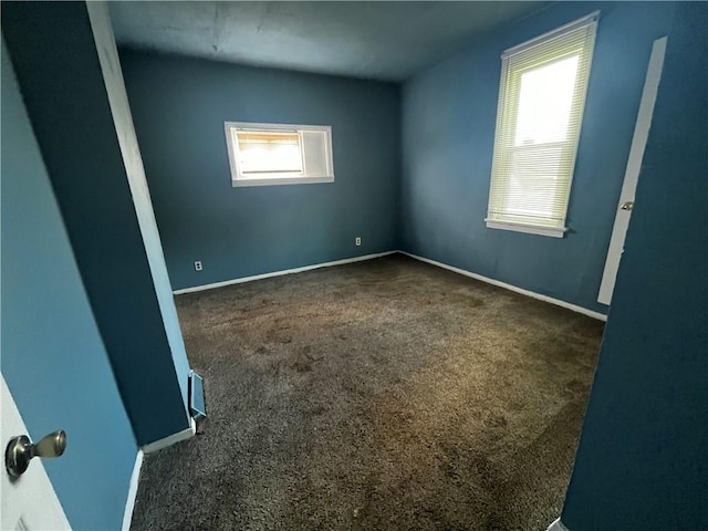 spare room with dark carpet, a healthy amount of sunlight, and baseboards