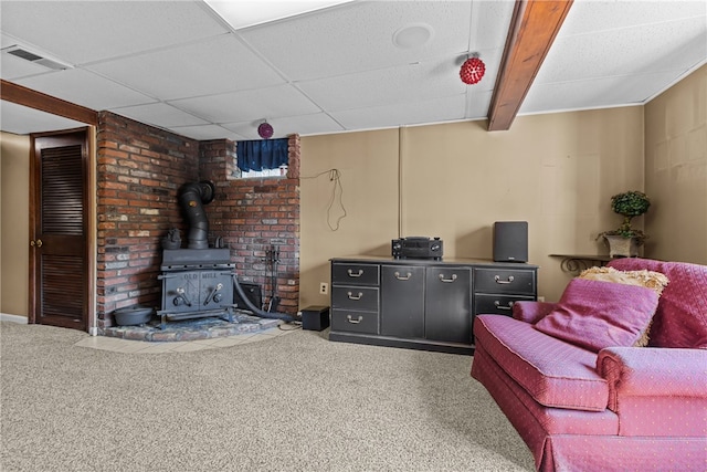 living room with carpet, a paneled ceiling, and a wood stove