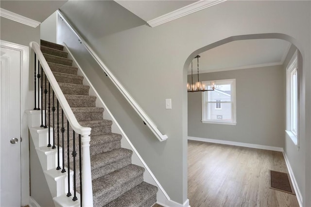 staircase with hardwood / wood-style floors, a notable chandelier, and ornamental molding