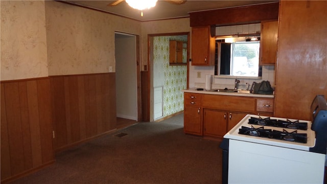 kitchen featuring wood walls, dark colored carpet, sink, white gas range oven, and ceiling fan