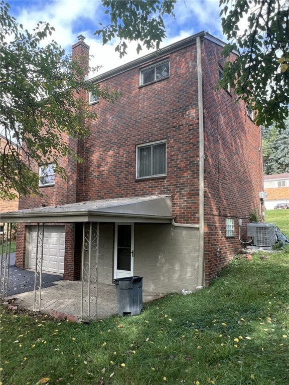 back of property featuring a garage, a lawn, and central air condition unit