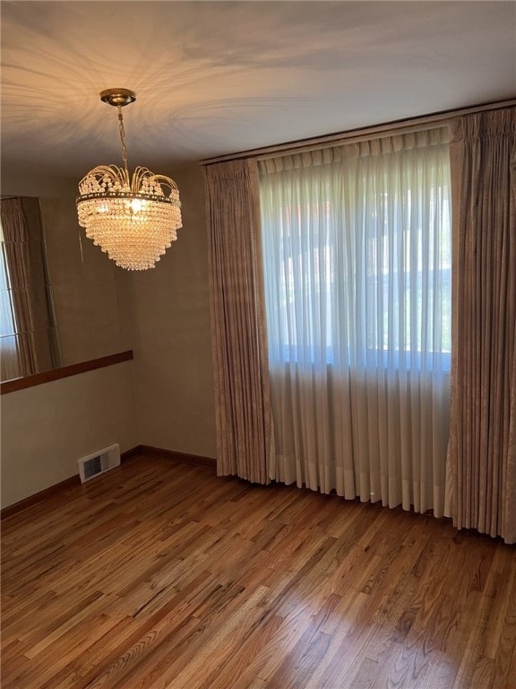 spare room featuring visible vents, baseboards, a chandelier, and wood finished floors