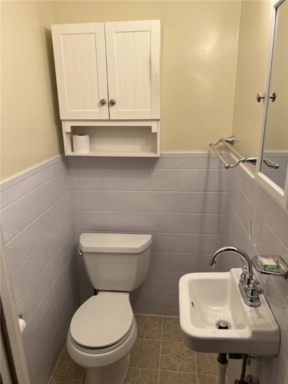 bathroom featuring a wainscoted wall, tile walls, a sink, and toilet
