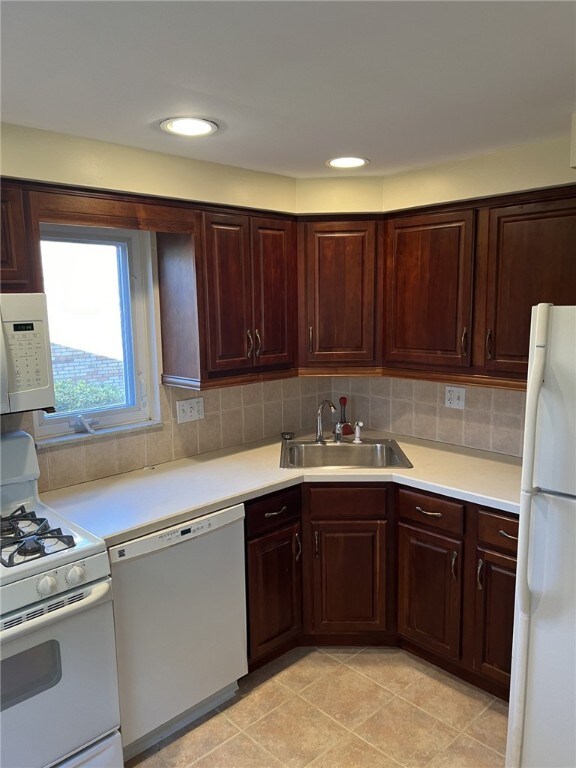 kitchen with a sink, light tile patterned floors, light countertops, and white appliances