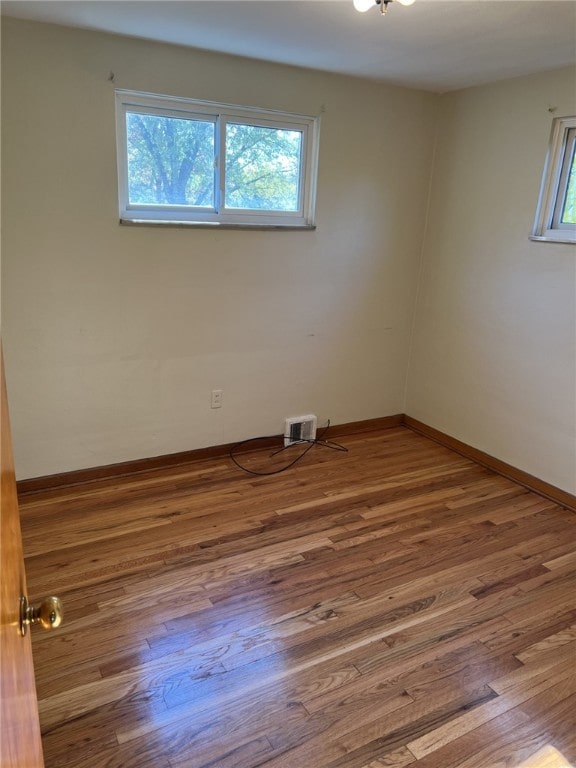 empty room with wood finished floors, baseboards, and visible vents