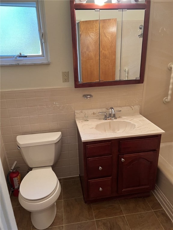 bathroom featuring a bath, tile patterned floors, toilet, vanity, and tile walls