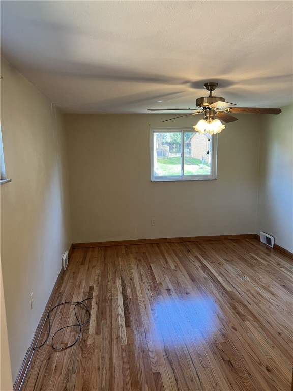 empty room featuring wood finished floors, ceiling fan, baseboards, and visible vents