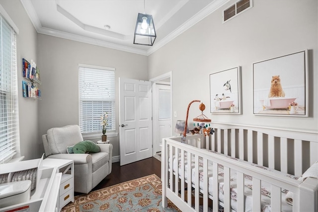 bedroom featuring dark hardwood / wood-style floors, a raised ceiling, a crib, and ornamental molding