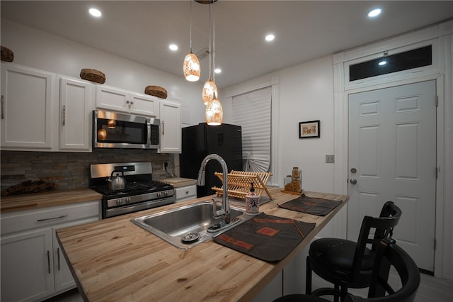 kitchen with white cabinets, appliances with stainless steel finishes, wood counters, and an island with sink