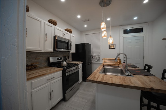 kitchen featuring sink, hanging light fixtures, wooden counters, an island with sink, and appliances with stainless steel finishes