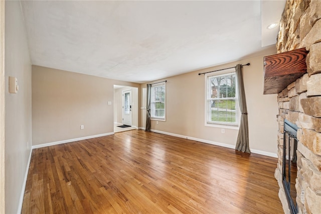 unfurnished living room featuring hardwood / wood-style flooring and a stone fireplace