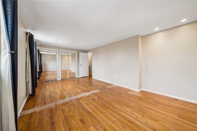 unfurnished bedroom with light hardwood / wood-style floors and multiple closets