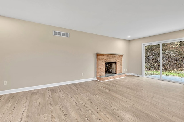 unfurnished living room with a brick fireplace and light hardwood / wood-style flooring