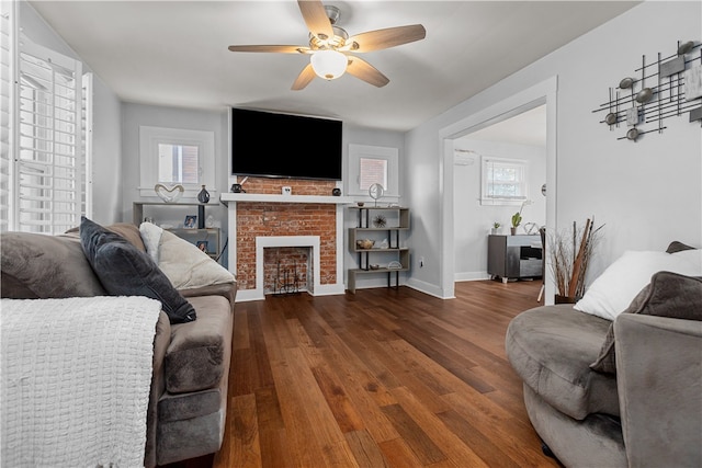 living room featuring ceiling fan, a healthy amount of sunlight, dark hardwood / wood-style floors, and a brick fireplace